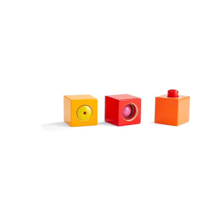 Drei Holzklötze sind in einer Reihe auf einem weißen Hintergrund abgebildet. Jeder Block hat eine andere Farbe - gelb, rot und orange - und jeder hat eine andere Form und ein anderes Objekt im Inneren oder auf der Oberseite.