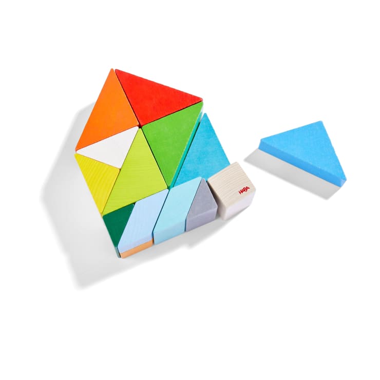 Bunte geometrische Holzblöcke sind in einem Muster auf einer weißen Fläche angeordnet, wobei ein blauer dreieckiger Block von der Hauptgruppe getrennt ist. Die Blöcke enthalten Dreiecke, Rechtecke und Quadrate.