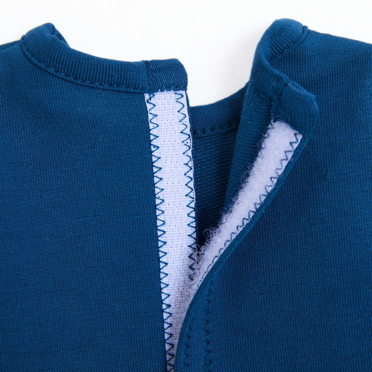 Nahaufnahme eines blauen Kleidungsstücks mit einem Klettverschluss, der auf der Rückseite teilweise geöffnet ist und Zickzacknähte entlang der Ränder erkennen lässt.