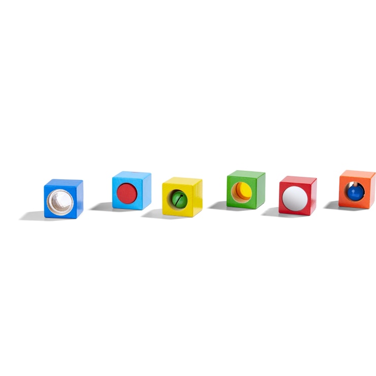 Sechs bunte Holzklötze sind in einer Reihe aufgereiht, wobei jeder Klotz eine andere Farbe und ein einzigartiges sensorisches Element oder Objekt auf einer Seite aufweist. Der Hintergrund ist weiß.