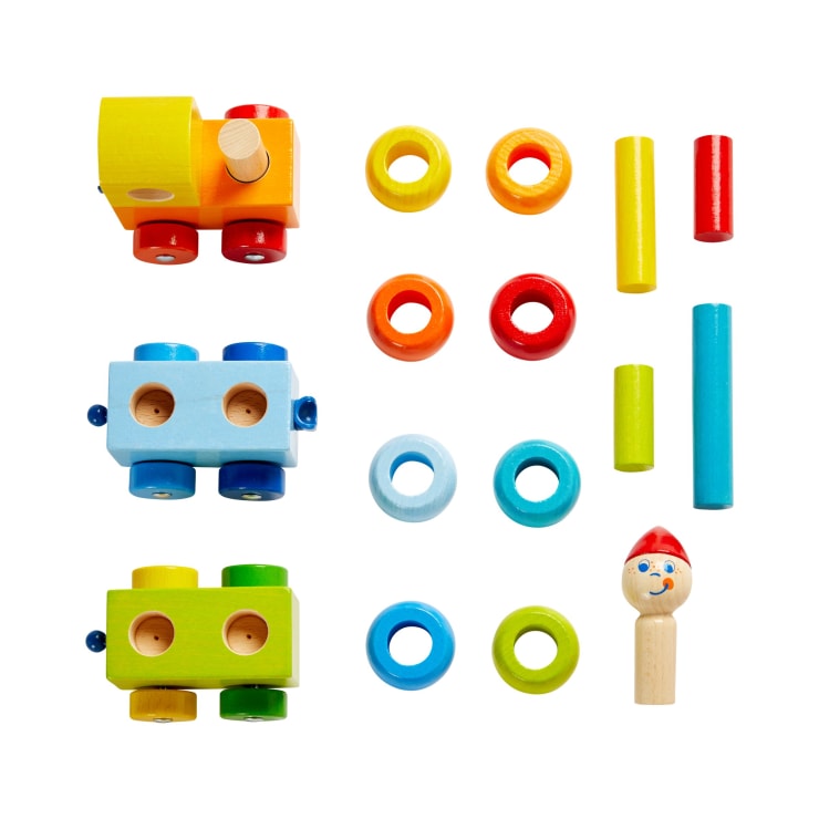 Eine Reihe von bunten hölzernen Spielzeugeisenbahnteilen und Ringen, die ordentlich auf einem weißen Hintergrund angeordnet sind, einschließlich Zugsockeln, kreisförmigen Ringen, zylindrischen Stäben und einer Zapfenpuppenfigur mit bemaltem Gesicht und roter Mütze.