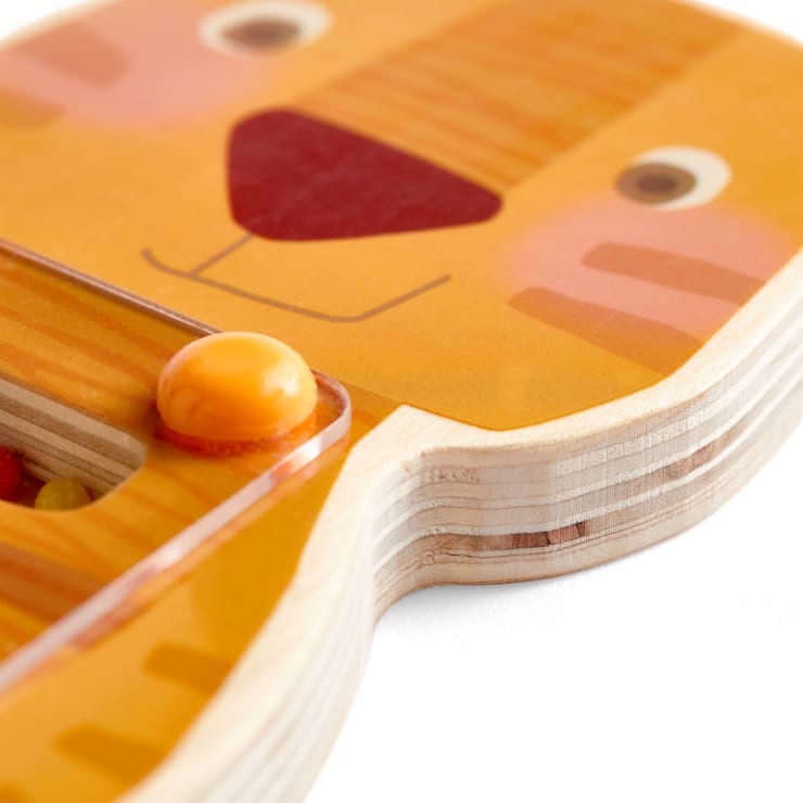 Eine Nahaufnahme eines Holzspielzeugs mit dem abgebildeten Gesicht eines Löwen, mit orange, gelb und rot bemalten Details und einer gebogenen Kante, die die geschichtete Holzkonstruktion des Spielzeugs zeigt.