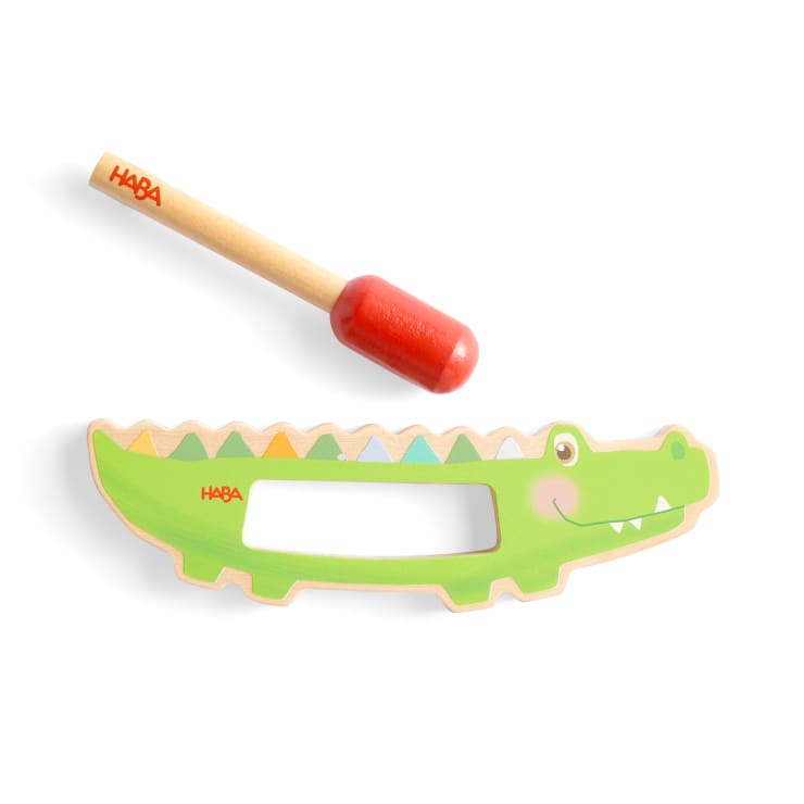 Ein Holzspielzeug in Form eines grünen Krokodils mit rechteckigem Ausschnitt und ein separater Holzhammer mit rotem Kopf und natürlichem Griff, beide mit HABA beschriftet.