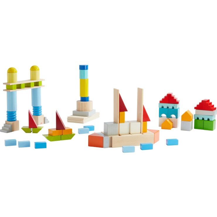 Mehrere bunte Holzbausteine werden zu verschiedenen geometrischen Strukturen zusammengesetzt, darunter Türme, Bögen, Boote mit roten Segeln und kleine Häuser, die alle auf einem weißen Hintergrund angeordnet sind.