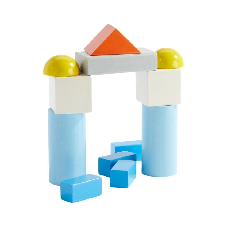 Ein Bauwerk aus Holzklötzen mit zwei blauen Zylindern als Säulen, zwei gelben Halbkugeln, einem grauen Rechteck, einem orangefarbenen Dreieck an der Spitze und mehreren kleinen blauen rechteckigen Klötzen an der Basis, alles auf weißem Hintergrund.