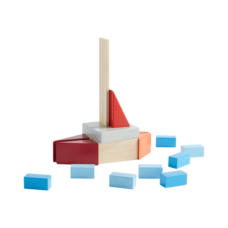 Eine Gruppe von bunten Holzbausteinen, die in Form eines Segelboots angeordnet sind, mit einem hohen vertikalen Stück als Mast, umgeben von mehreren verstreuten blauen Blöcken auf weißem Hintergrund.
