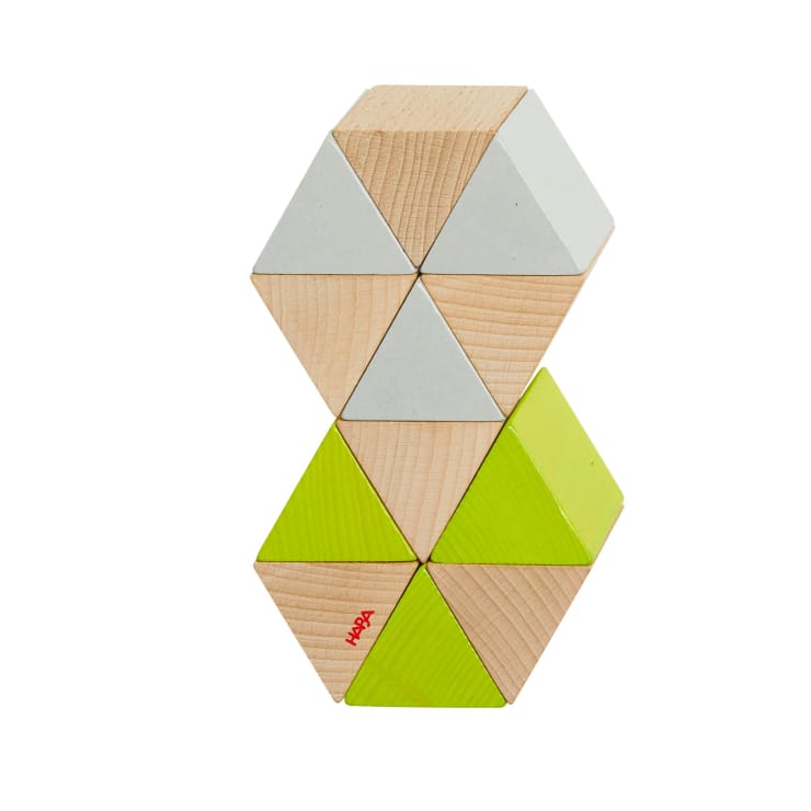 Ein Set aus dreieckigen Holzklötzen, die in einem vertikalen sechseckigen Stapel angeordnet sind, mit naturfarbenen, weißen und grünen Teilen. Ein grünes Dreieck ist mit dem Wort HABA in Rot bedruckt.