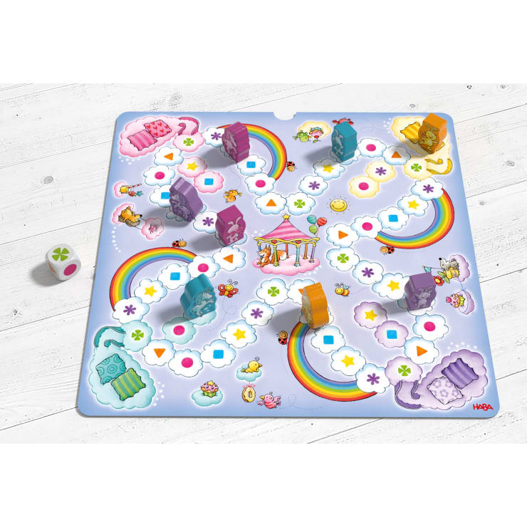 Ein farbenfrohes Brettspiel mit Regenbögen, Tieren und einem Karussell in der Mitte, mit orangefarbenen und lilafarbenen Spielfiguren und einem weißen Würfel mit farbigen Symbolen, auf einer weißen Holzoberfläche.