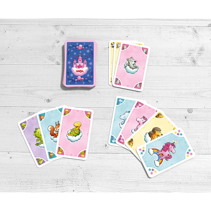 Ein Kartenspiel mit einem Schlossmotiv auf der Rückseite liegt auf einer weißen Holzfläche. Mehrere Kartenblätter mit bunten Tieren auf Wolken sind auf dem Deck verteilt.