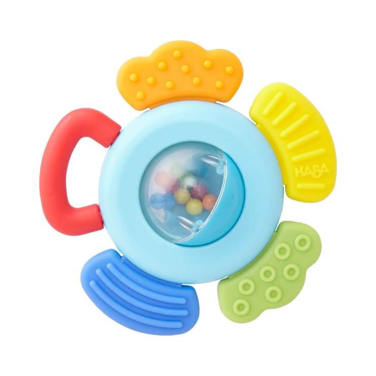 Eine farbenfrohe Babyrassel mit einem kreisförmigen blauen Zentrum, das kleine bunte Perlen enthält, vier strukturierten Klappen in Gelb, Grün und Blau und einem roten Griff an einer Seite.