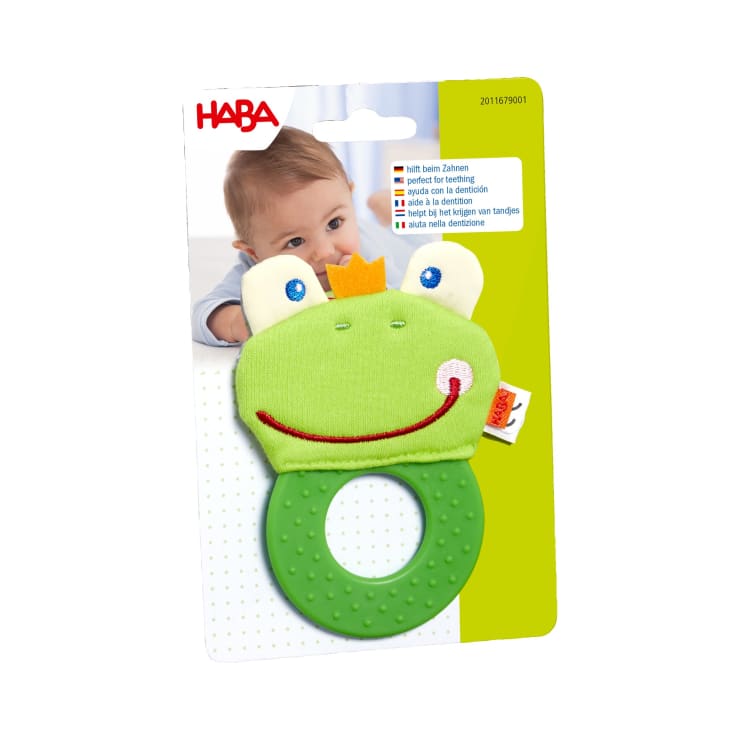 Ein grünes Beißspielzeug in Form eines Frosches mit einem strukturierten Ring, verpackt auf einer Karte mit dem Gesicht eines Babys und Produktinformationen in mehreren Sprachen. Der Markenname HABA ist oben links zu sehen.