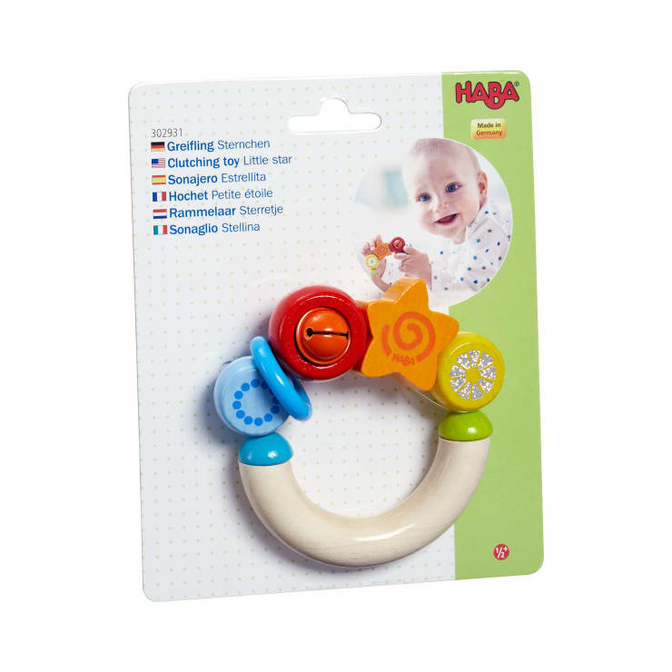Ein verpacktes HABA Greifspielzeug für Babys in Form eines Rings mit bunten Perlen und einem Stern. Die Verpackung zeigt ein Baby und Text in mehreren Sprachen, darunter Englisch, Deutsch und Spanisch.