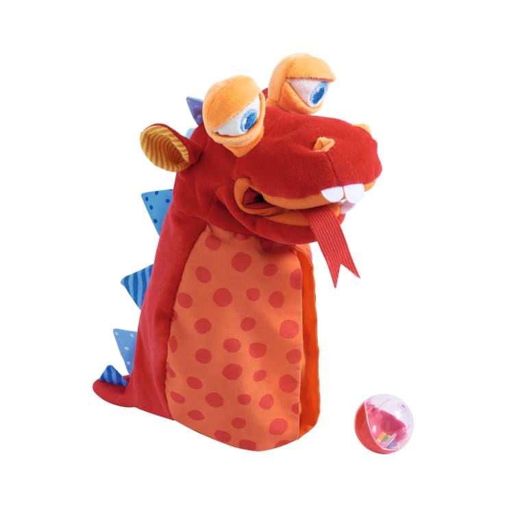 Eine weiche, farbenfrohe Drachenhandpuppe mit orangefarbenen und roten Punkten, blauen Stacheln auf dem Rücken und einer roten Filzzunge, die neben einer kleinen transparenten Kugel mit einem Spielzeug steht.