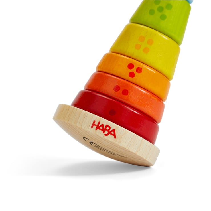 Ein buntes Stapelspielzeug aus Holz mit sechs Ringen in Grün-, Gelb-, Orange- und Rottönen auf einem runden, gekippten Holzsockel mit der Aufschrift HABA. Die Ringe haben Punkte in passenden Farben.