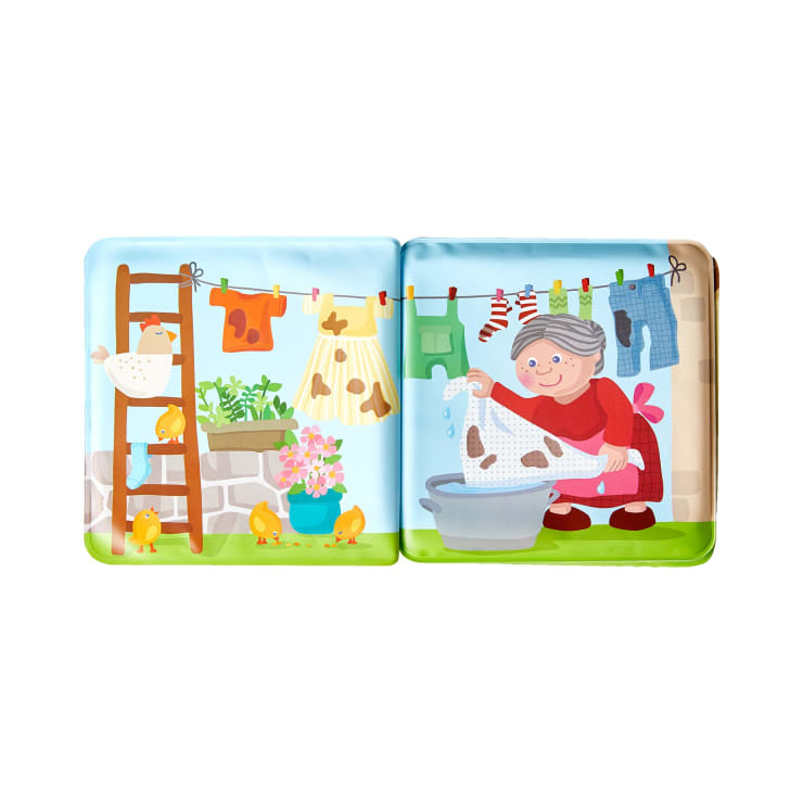 Eine illustrierte Kinderbuchseite zeigt eine ältere Frau, die Wäsche in einer Schüssel wäscht, während in der Nähe Wäsche auf einer Leine hängt, Blumen in einem Topf, eine Leiter, eine Henne und mehrere gelbe Küken.