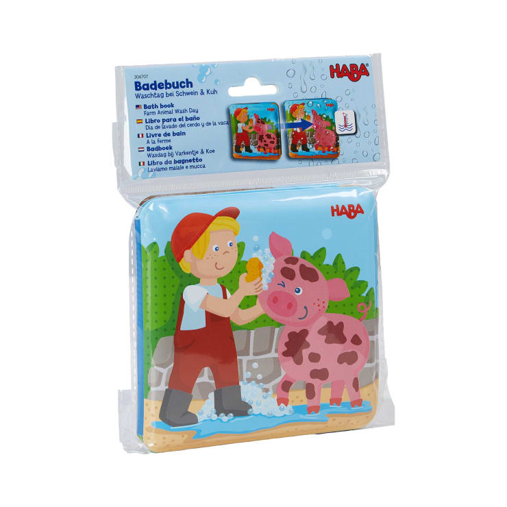 Ein verpacktes HABA-Badebuch mit dem Titel WaschLab die Schwein & Kuh zeigt ein Kind in roter Latzhose und Mütze, das im Freien ein rosa Schwein mit Wasser und Seife wäscht.