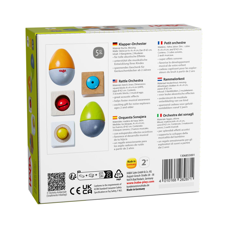 Rückseite einer Spielzeugschachtel mit Abbildungen von zwei eiförmigen Musikspielzeugen in orange-gelb und grün-grau sowie zwei Holzsockeln mit roten und blauen Kreiselementen. Der Text in mehreren Sprachen beschreibt das Produkt für Kinder ab 2 Jahren.