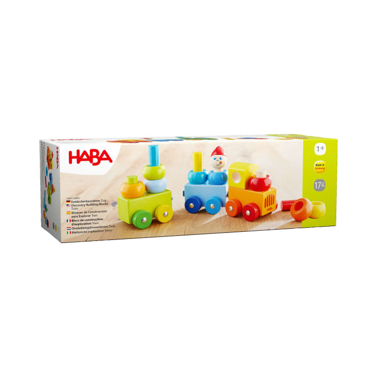 Eine rechteckige Schachtel der HABA-Holzspielzeugeisenbahn für Kinder ab 1 Jahr. Sie zeigt einen bunten Zug mit gelben, blauen und grünen Teilen und einer kleinen Figur. Die Verpackung enthält Produktinformationen in mehreren Sprachen.