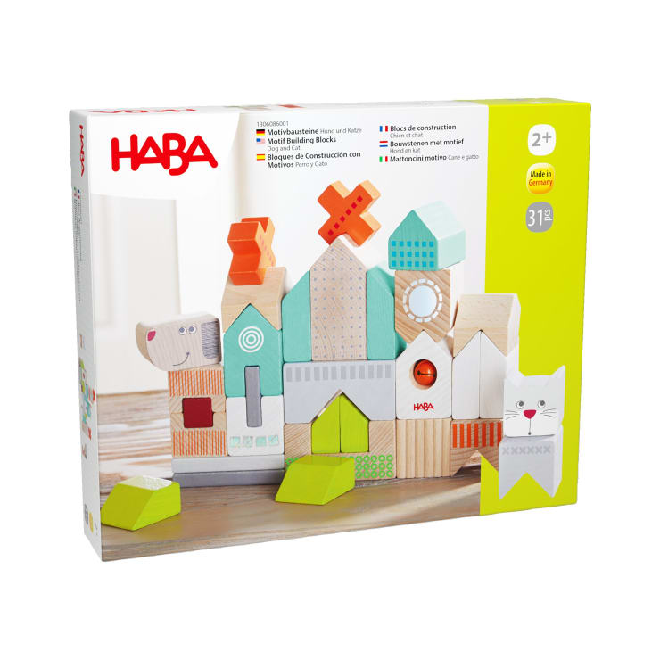 Eine Schachtel mit HABA-Motiv-Bauklötzen für Kinder ab 2 Jahren. Die Schachtel zeigt bunte Holzklötze, die in verschiedenen Formen angeordnet sind, darunter Tiere und geometrische Formen. Das Set enthält 31 Teile und wird in Deutschland hergestellt.