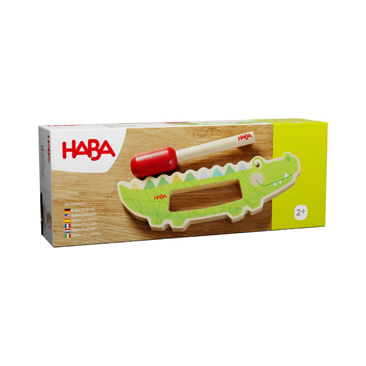 Rechteckige Schachtel mit einem Krokodil-Holzspielzeug der Marke HABA mit einem roten und natürlichen Holzschläger. Auf der Verpackung ist ein lächelndes grünes Krokodil abgebildet und das Spielzeug ist für Kinder ab 2 Jahren geeignet.