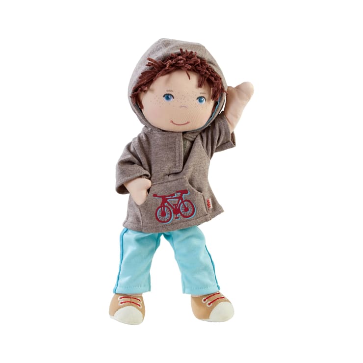 Eine weiche Puppe mit braunen Haaren, blauen Augen und Sommersprossen trägt einen grauen Kapuzenpullover mit roter Fahrradgrafik, hellblaue Hosen und braune Schuhe. Der rechte Arm der Puppe ist erhoben und sie steht auf einem schlichten weißen Hintergrund.
