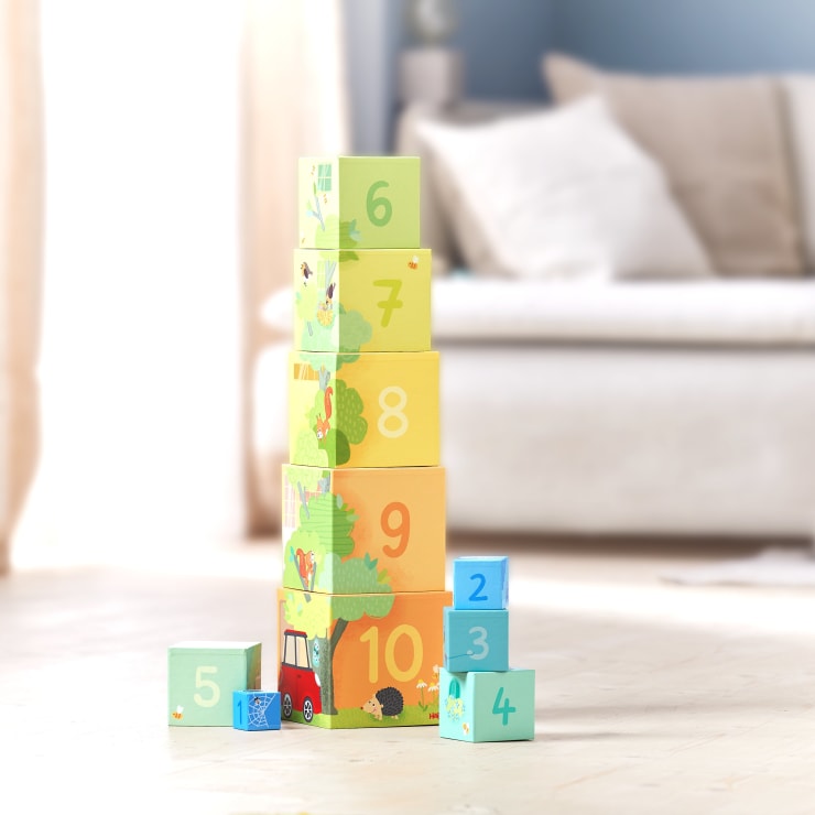 Ein Stapel bunter nummerierter Blöcke, angeordnet vom größten unten mit der Bezeichnung 10 bis zum kleinsten oben mit der Bezeichnung 6, mit einem Sofa und weichen Möbeln im unscharfen Hintergrund.
