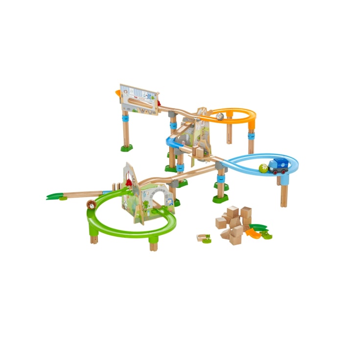 Ein hölzernes Murmelbahn-Spielzeugset mit erhöhten Bahnen in Grün, Blau und Orange, mit Rampen, Blöcken und verschiedenen Verbindungsstücken sowie mehreren losen Teilen auf weißem Hintergrund.