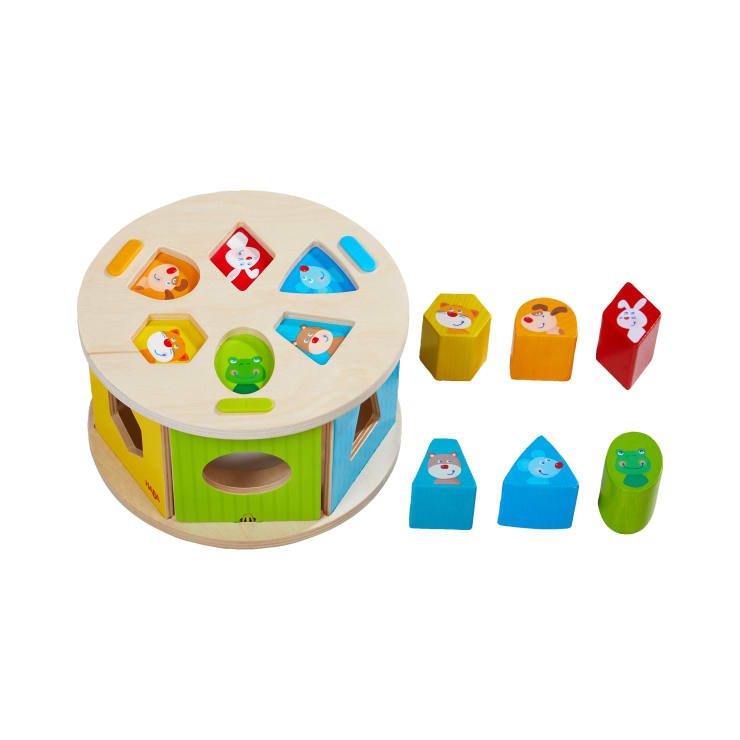 Ein hölzernes Formen-Sortierspielzeug mit Tiergesichtern, das eine runde Basis mit verschieden geformten Löchern und passenden bunten Blöcken daneben aufweist. Jeder Block hat eine andere Form und ein anderes Tiermotiv.
