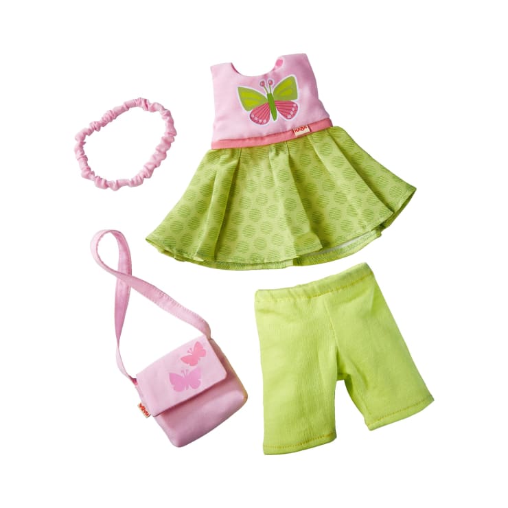 Ein Puppen-Outfit-Set mit einem rosa und grünen Kleid mit Schmetterlingsaufdruck, einem passenden rosa Haargummi, einer rosa Umhängetasche mit Schmetterlingsmotiven und hellgrünen Shorts, alles auf weißem Hintergrund.