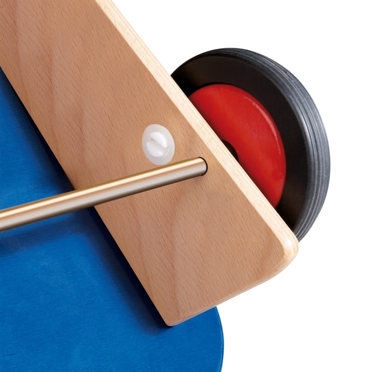 Nahaufnahme einer Holzstruktur mit einer Metallstange, einem an einem Ende angebrachten rot-schwarzen Rad und einer blauen flachen Oberfläche, die teilweise vor einem weißen Hintergrund sichtbar ist.