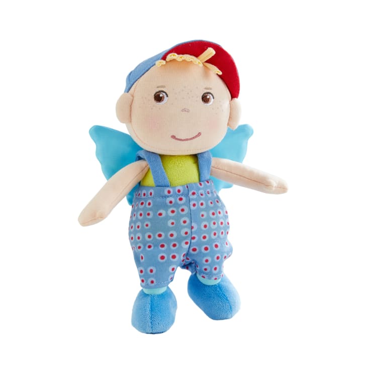 Plüschpuppe mit blauer Mütze, hellgrünem Hemd und blauer Latzhose mit roten und weißen Punkten. Die Puppe hat helle Haut, aufgenähte Gesichtszüge und blaue Stoffflügel auf dem Rücken.