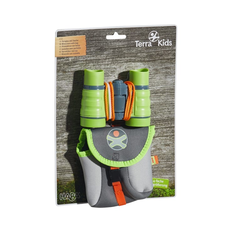 Ein Paket mit einem grünen und grauen Fernglas mit einer orangefarbenen Kordel, das über einer passenden grauen Tragetasche mit einer orangefarbenen Schnalle ausgestellt ist. Die Verpackung ist mit Terra Kids und HABA auf einem hölzernen Hintergrund beschriftet.