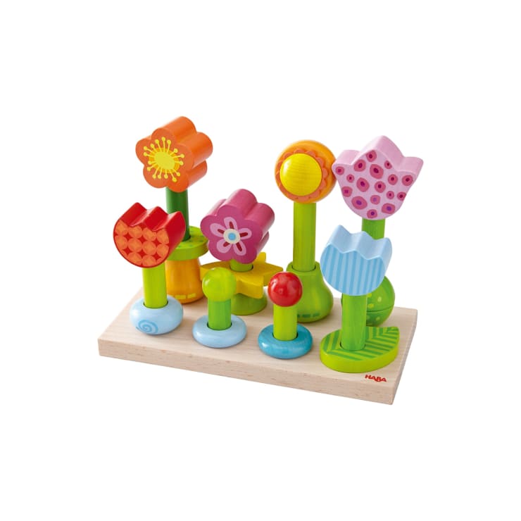 Ein Holzspielzeugset mit bunten, stapelbaren Blumen auf grünen Stielen, die aufrecht auf einem rechteckigen Holzsockel angeordnet sind. Die Blumen haben verschiedene Formen und Farben, darunter rot, rosa, gelb und blau.
