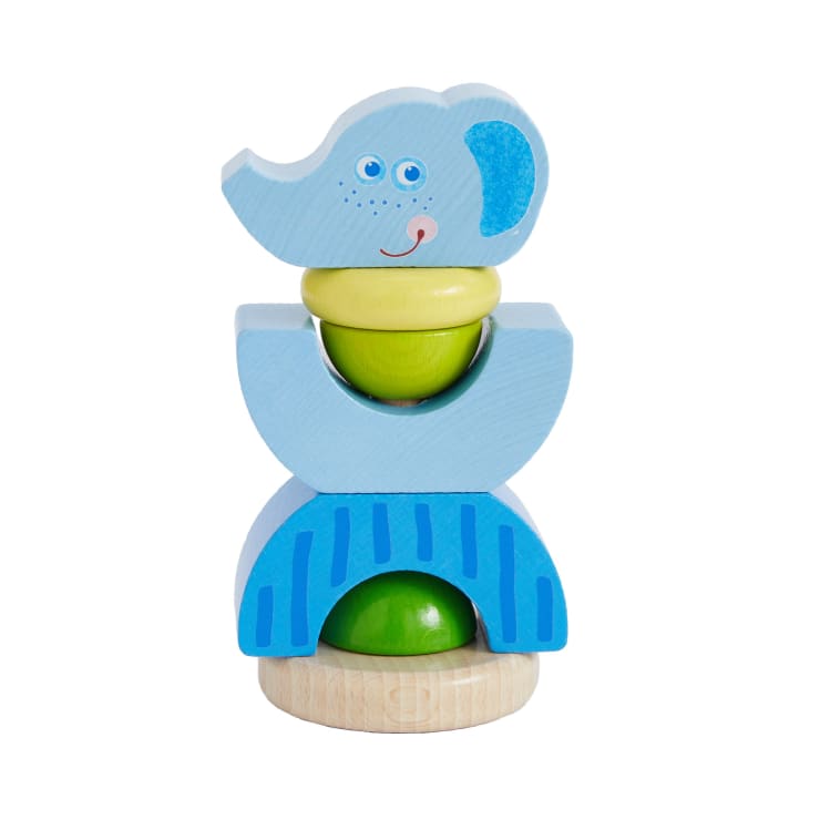 Ein Stapel bunter Holzspielzeugteile, darunter blaue, grüne und gelbe Formen, wobei das oberste Teil wie ein Elefantenkopf mit einem lächelnden Gesicht und blauen Ohren geformt und bemalt ist.