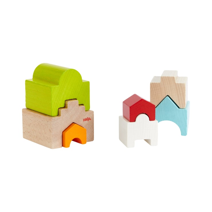 Zwei Sätze von Holzstapelblöcken sind auf einem weißen Hintergrund angeordnet. Das linke Set besteht aus grünen, beigen und orangefarbenen Blöcken, während das rechte Set aus roten, weißen, blauen und naturfarbenen Holzblöcken besteht.