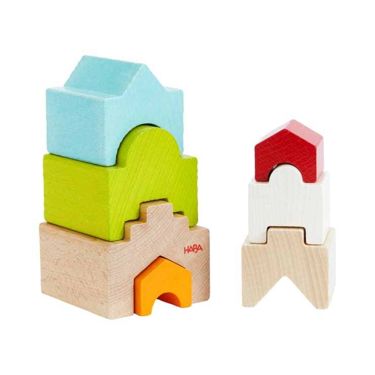 Zwei Stapel mit bunten Holzbausteinen in Form von Häusern. Der linke Stapel besteht aus vier Klötzen in den Farben Blau, Grün, Naturholz und Orange. Der rechte Stapel besteht aus drei Klötzen in den Farben Rot, Weiß und Naturholz.