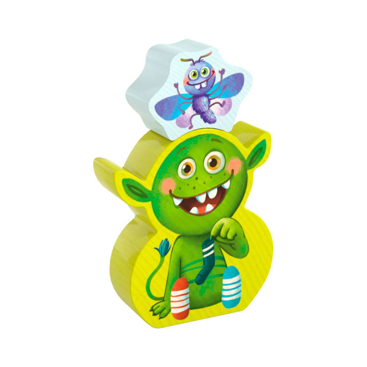 Ein Holzspielzeug mit einem grünen Wesen mit großen Augen, spitzen Ohren und unpassenden Socken, das seinen Fuß festhält. Ein separater weißer Block mit einer Illustration eines lila insektenähnlichen Wesens sitzt obenauf.