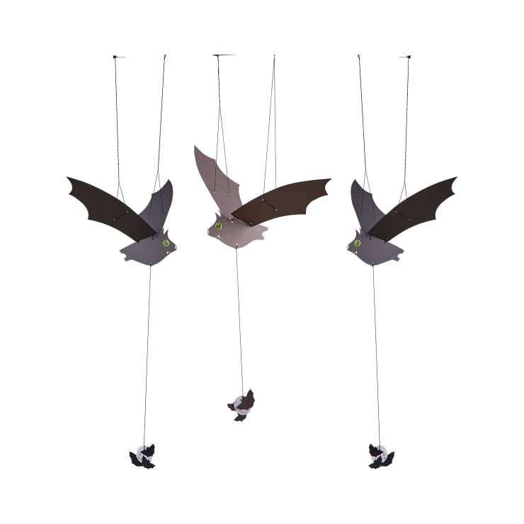 Drei hängende Fledermausdekorationen mit ausgestreckten Flügeln, die an Schnüren von der Decke hängen, mit jeweils einer kleinen Fledermaus darunter. Die Fledermäuse haben Cartoon-Augen und sind auf einem schlichten weißen Hintergrund zu sehen.