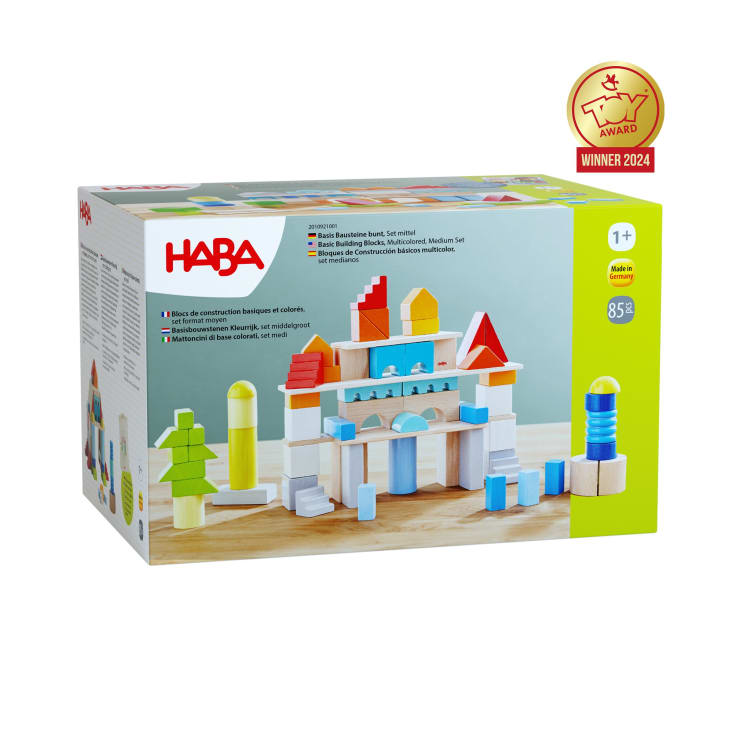 Abgebildet ist eine Schachtel mit HABA-Grundbausteinen mit bunten Holzteilen. Die Verpackung zeigt ein zusammengesetztes Bauwerk und eine Plakette des Toy Award 2024. Das Spielzeug ist für Kinder ab 1 Jahr geeignet und enthält 85 Teile.