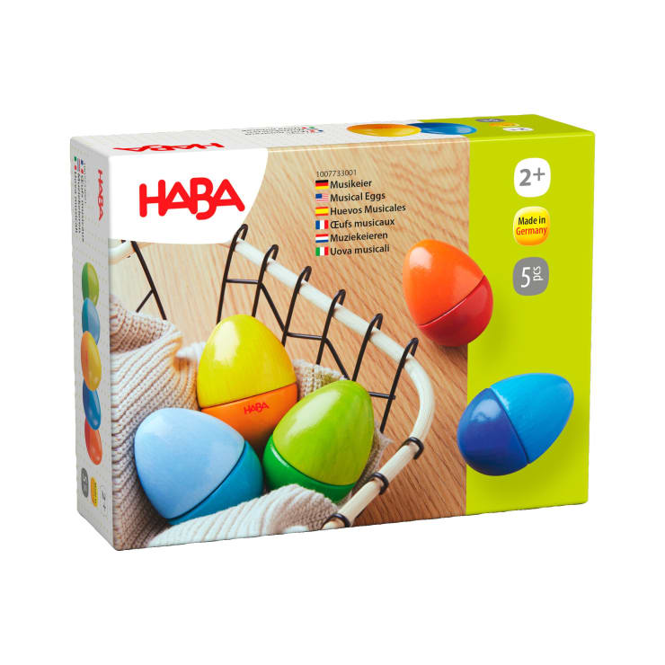 Eine Schachtel mit HABA-Musik-Eiern für Kinder ab 2 Jahren mit fünf bunten Eiern in den Farben blau, gelb, orange, grün und rot, mit einem Korb und einem gestrickten Tuch auf der Verpackung.