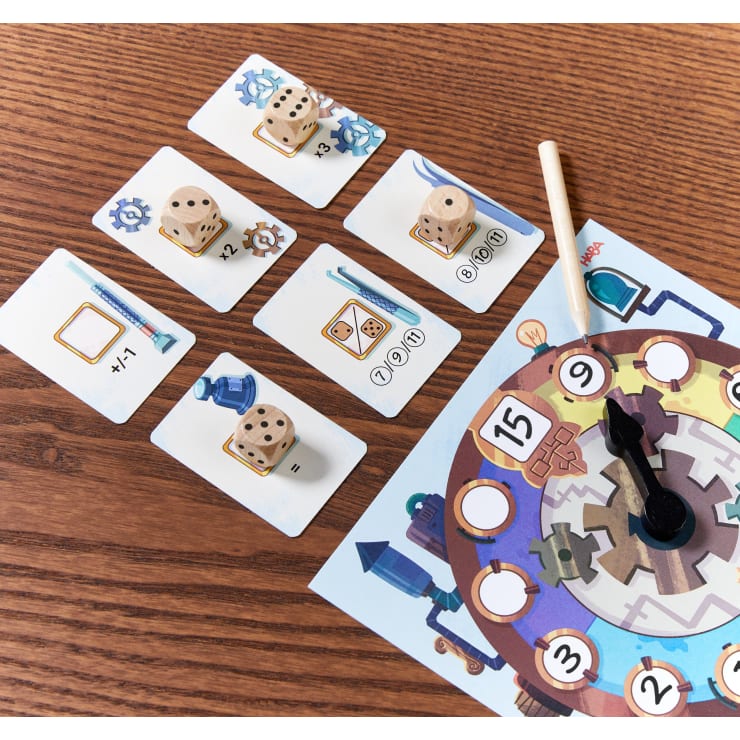 Vier illustrierte Spielkarten mit Würfeln und Zahnradsymbolen liegen auf einem Holztisch neben einem Teil eines runden Spielbretts mit einer nummerierten Strecke und einem auf 9 eingestellten Pappdreher. In der Nähe liegt ein Holzstab.