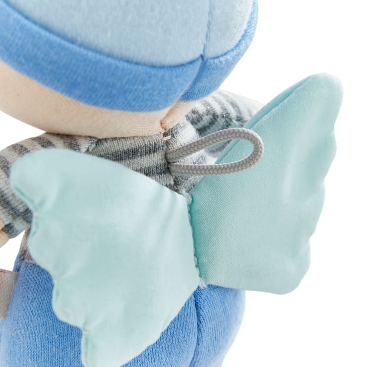 Nahaufnahme einer Stoffpuppe mit hellblauem Hut, grau-weiß gestreiftem Oberteil und weichen blauen Flügeln, die mit einer weißen Gummischlaufe am Rücken befestigt sind. Das Bild ist von hinten aufgenommen.