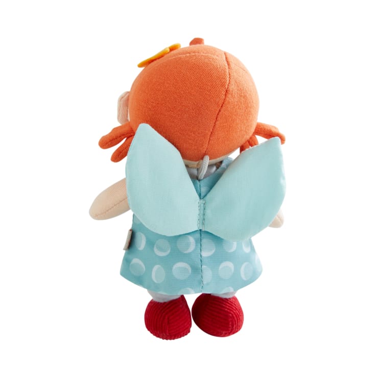 Plüschpuppe mit orangefarbenen Haaren, hellblauem Kleid mit weißen Tupfen, blauen Flügeln und roten Schuhen, von hinten vor weißem Hintergrund dargestellt.