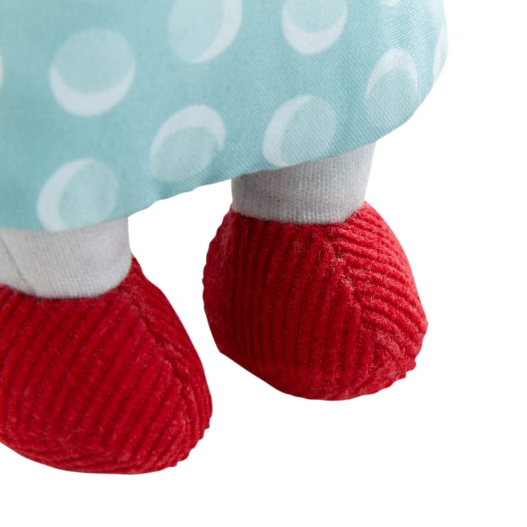 Nahaufnahme der Unterschenkel und Füße einer Puppe, die einen hellblauen Rock mit weißen Tupfen und leuchtend rote, strukturierte Schuhe trägt.