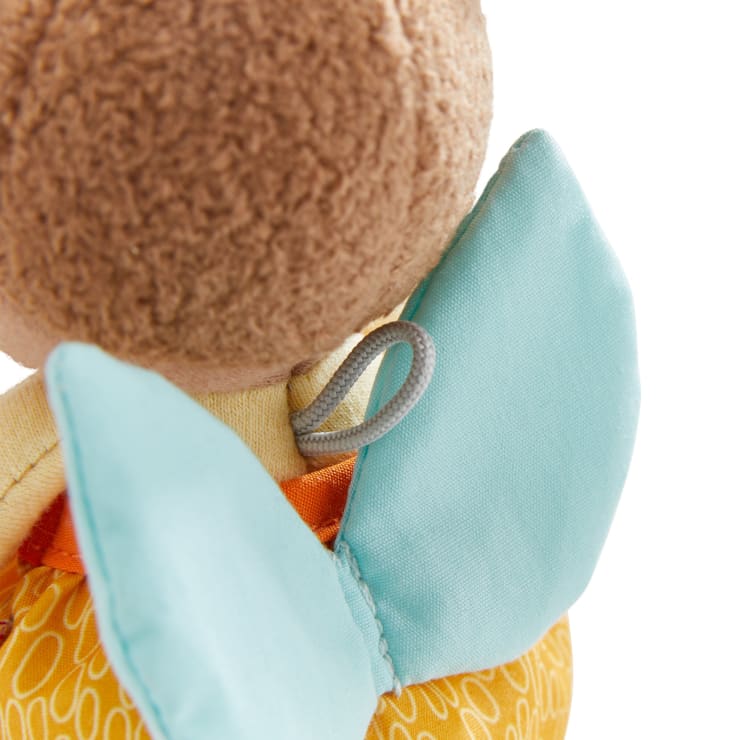 Nahaufnahme eines Plüschtiers, die den Hinterkopf, zwei hellblaue Stoffflügel und einen Teil des gelben Körpers mit weißem Schnörkelmuster vor weißem Hintergrund zeigt.