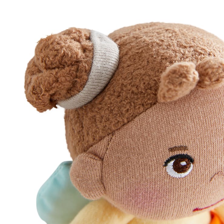 Eine Nahaufnahme von Gesicht und Haar einer Stoffpuppe, die braunes, strukturiertes Haar zeigt, das zu einem Dutt mit einem grauen Haarband gestylt ist, gestickte braune Augen und einen Teil eines hellblauen Accessoires im Hintergrund.