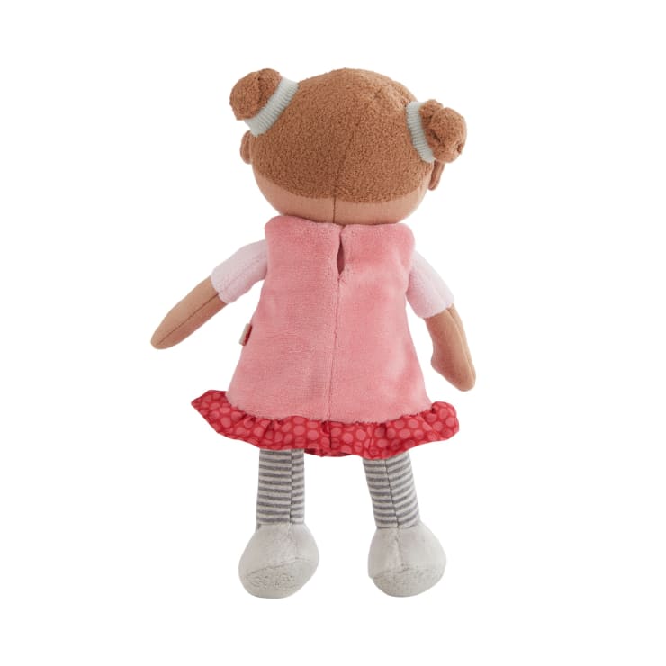 Eine Plüschpuppe, von hinten gesehen, mit hellbrauner Stoffhaut, braunen Haaren, die zu zwei Dutts gestylt sind, einem rosa-roten Kleid, gestreiften Leggings und weißen Schuhen.