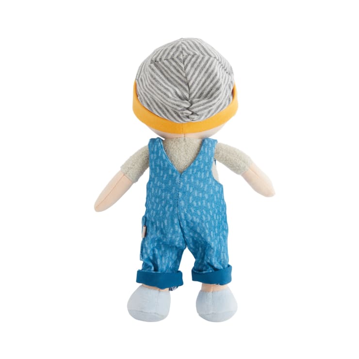 Eine Plüschpuppe mit Blickrichtung nach außen, die einen grau-weiß gestreiften Hut mit gelbem Band, ein helles Hemd, eine blaue Latzhose mit einem Muster und hellblaue Schuhe trägt, isoliert auf weißem Hintergrund.