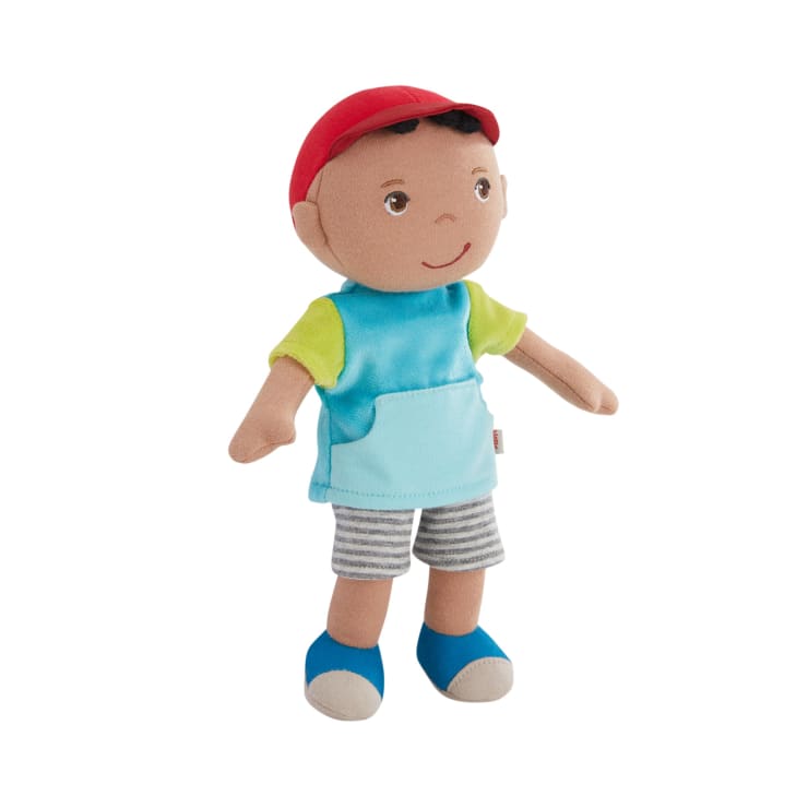 Eine weiche Stoffpuppe mit roter Mütze, blau-grünem Hemd, grau gestreiften Shorts und blauen Schuhen, die aufrecht vor einem weißen Hintergrund steht.