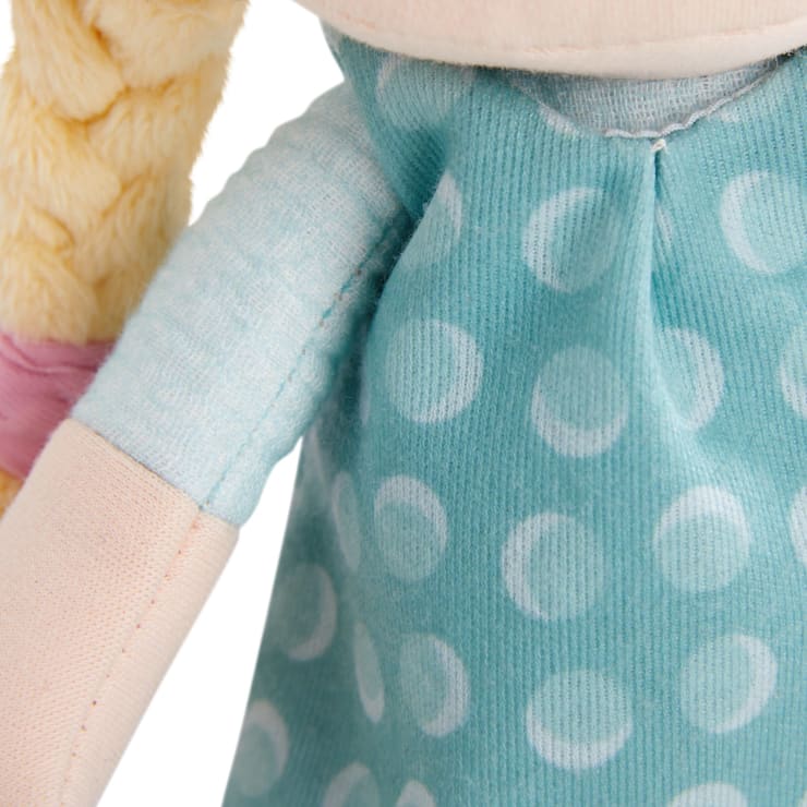 Nahaufnahme einer Plüschpuppe, die ein blaues Kleid mit weißen Tupfen trägt. Nur der Oberkörper, ein Teil des Arms und einige hellbraune Haare, die mit einem rosa Band geflochten sind, sind sichtbar.